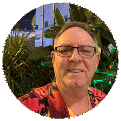 Lächelnder Mann mit Brille und rotem Hawaii-Hemd vor tropischer Pflanzenkulisse